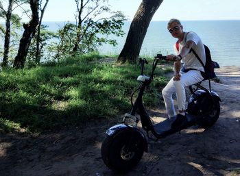Full length of man sitting by sea on motor scooter