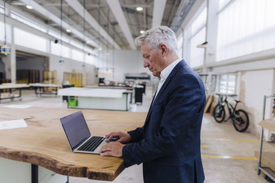 Businessman using laptop on workbench in factory