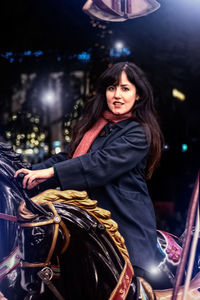 Portrait of smiling young woman standing in city at night