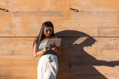 Young asian girl leaning against a wall using her tablet.