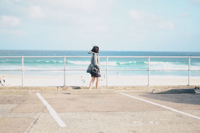 Rear view of woman standing by sea against sky