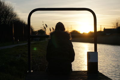 Rear view of woman sitting by lake during sunset
