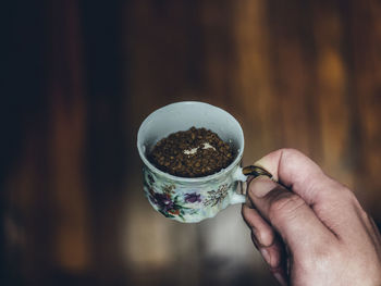 Close-up of hand holding coffee cup against wooden floor - retro edit