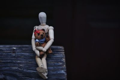 Close-up of figurine with toy on log against black background