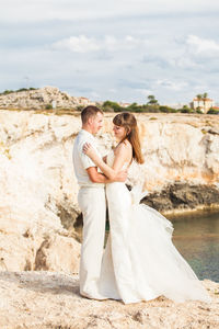 Couple embracing while standing by sea against sky