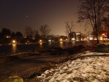 Illuminated street by canal against sky at night