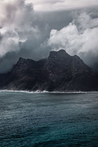 Scenic view of sea by mountain against sky