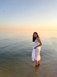 Rear view of woman standing at beach against sky during sunset