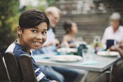 Happy boy looking away while sitting with family at dining table in yard