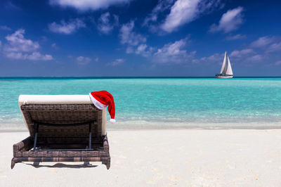 Santa hat on lounge chair at beach against blue sky