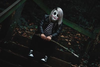 Portrait of man wearing mask while sitting on steps in forest