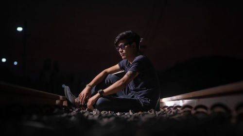 Surface level of young man sitting on gravels against sky at night