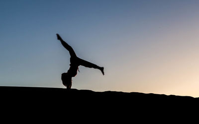 Low angle view of silhouette woman practicing handstand against clear sky during sunset