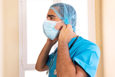 Side view of male medic in uniform putting on disposable mask during work in clinic