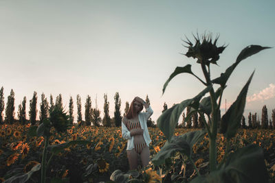 Woman standing in bikini at sunflower farm against sky