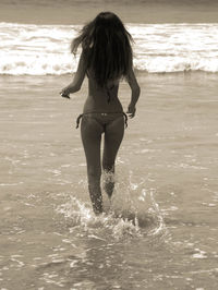 Rear view full length of woman in bikini running at beach