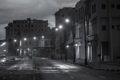 Illuminated city street by buildings at night