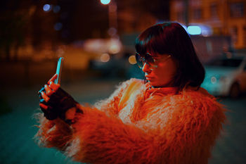 Woman taking selfie while standing in city at night