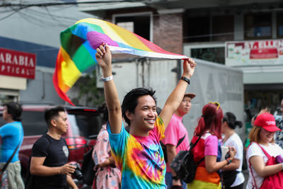 Smiling man holding rainbow flag while standing in city