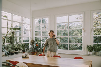 Mid adult woman talking on smart phone looking away while standing at home