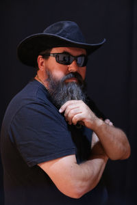 Portrait of bearded mature man wearing sunglasses against black wall