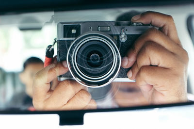 Cropped hands of man photographing with camera reflecting on rear-view mirror in car