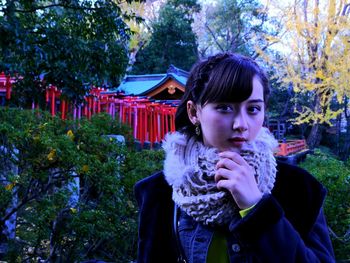 Portrait of young woman standing against trees in park