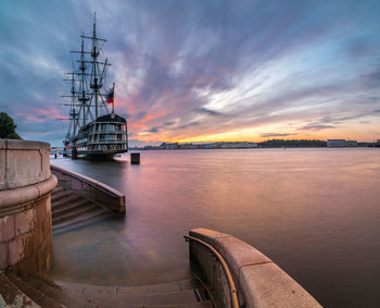Ship moored at harbor against sky during sunset