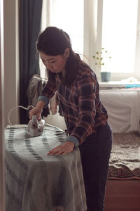 Woman irons at home, routine housekeeping and ironing in apartment, domestic cleaning of household