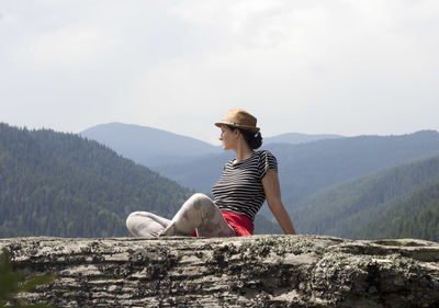 Full length of woman sitting on mountain rock against sky