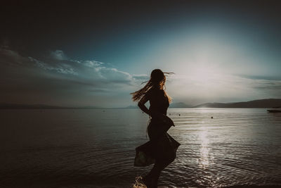 Silhouette woman standing at beach against sky during sunset