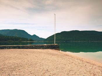 Stony sporty port at mountain lake. end of wharf with empty pole without flag.