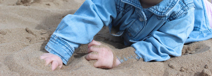 Midsection of child lying on sand at beach