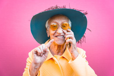 Senior woman wearing hat talking over smart phone against pink background