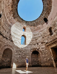 Man standing inside ancient roman building with natural light shining on him.