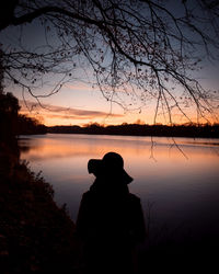 Silhouette person looking at lake against sky during sunset