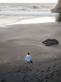 Young woman walking on a rocky beach, looking at view