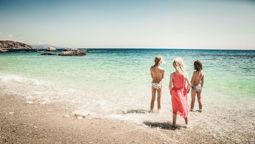 Rear view of women standing at beach against sky