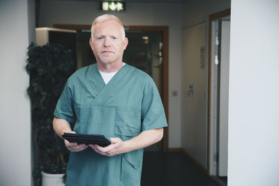 Portrait of confident mature male nurse holding digital tablet at hospital corridor