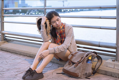 Young woman looking down while sitting on railing