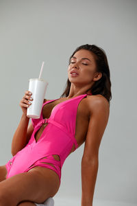 Portrait of young woman drinking water against white background