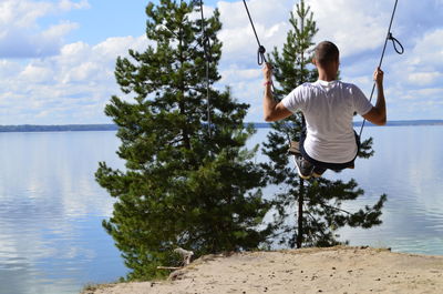 Rear view of man sitting on shore against sky