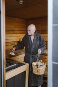 Senior man putting hot stone in heater machine while standing in sauna