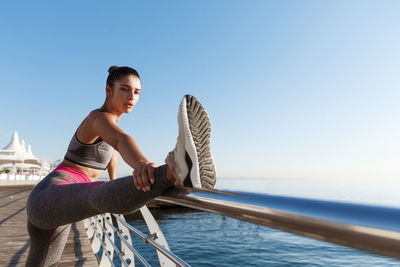 Young woman exercising by railing against sky