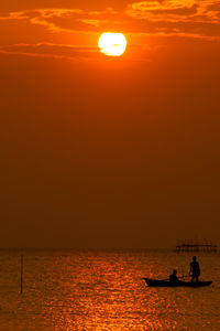 Silhouette people on sea against sky during sunset