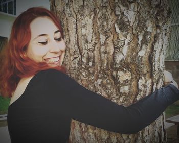 Portrait of smiling young woman against tree trunk