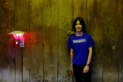 Portrait of smiling young woman standing against wooden wall