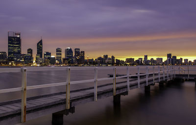 City by river against sky at dusk