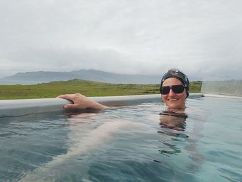 Portrait of smiling young woman swimming in water against sky