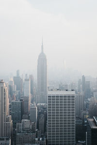 Empire state building amidst modern towers in city against sky